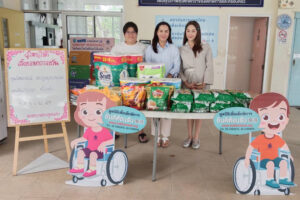 ผู้หญิง 3 คนยืนข้างกันด้านหน้ามีโต๊ะสีขาวมีสิ่งของว่างอยู่