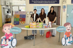 ผู้หญิง 4 คนยืนด้านหน้ามีโต๊ะวางสิ่งของบริจาค