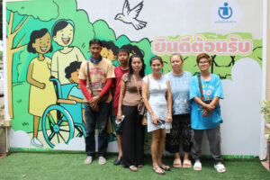 ผู้หญิงและและชายยืนถ่ายภาพร่วมกันด้านลังป้ายมูลนิธิเพื่อเด็กพิการ